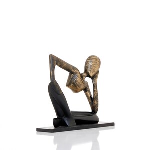May include: A gold and black abstract sculpture of a person sitting with their chin on their hand, as if in thought. The sculpture is on a black base.