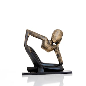 May include: A wooden sculpture of a person sitting with their head resting on their hand. The sculpture is painted in black and gold.