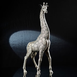 Könnte beinhalten: Eine silberfarbene Giraffenfigur mit einer strukturierten, gemusterten Oberfläche. Die Figur steht auf einer schwarzen Oberfläche.