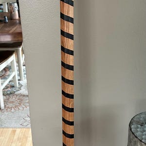 May include: A wooden walking stick with black stripes painted on it. The stick is made of light brown wood with a natural grain pattern.