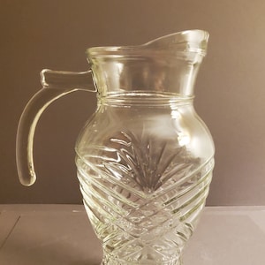 Może przedstawiać: Szklany dzbanek z przezroczystego szkła z wzorem diamentowym. Dzbanek ma szeroki otwór i uchwyt.