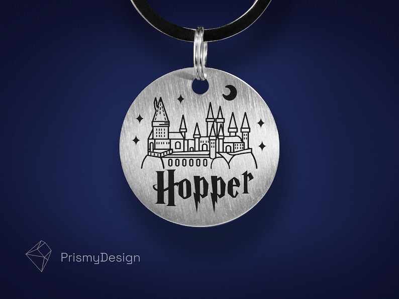 May include: A silver round tag featuring a black outline of Hogwarts castle, stars, and a crescent moon. The tag is engraved with the name "Hopper" in a black gothic font.