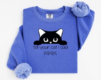 Può includere: Una felpa blu reale con un gatto nero che spunta dal bordo e il testo "tell your cat I said pspsps".