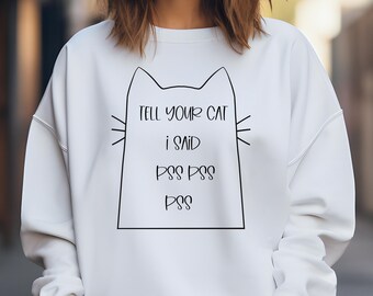 Può includere: Una felpa bianca a maniche lunghe con una grafica a linee nere che raffigura la sagoma di un gatto. All'interno della forma del gatto, il testo recita: TELL YOUR CAT I SAID PSS PSS PSS. La felpa presenta un girocollo e polsini a coste.