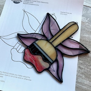 Pode incluir: Um padrão de vitral para um pincel com um design floral. O padrão tem 16,5 cm de comprimento e está em escala de 100%. O padrão foi projetado por Golden State Glassworks e é protegido por direitos autorais de 2004. O texto "Faerie Paintbrush" está no topo do padrão.