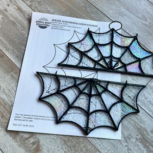 Pode incluir: Dois padrões de teia de aranha de vidro colorido, um com um cabide, em uma folha de papel branca com instruções. O papel inclui o texto "Spider Web Propagation Station", "Stained Glass Pattern", "Designed by Golden State Glassworks", "Copyright 2024", "@goldenstateglassworks", "You may sell any finished pieces you make from this pattern. The pattern itself is not to be sold or reproduced for sale", e "Size: 9.5" tall @ 100%".