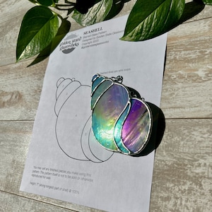 Puede incluir: Un patrón de concha de mar de vidrio coloreado con una guía de colores para las diferentes piezas. El patrón está diseñado por Golden State Glassworks y tiene 17,8 cm de alto.