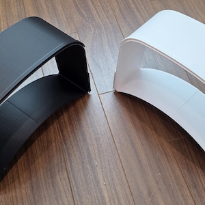 May include: Two modern, curved, shelf-like structures. One is matte black, the other is white. Both have a rounded top and bottom with an open interior. They sit on a wooden surface.