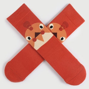 May include: A pair of orange socks with a cartoon animal design. The animal has brown, white, and orange features.