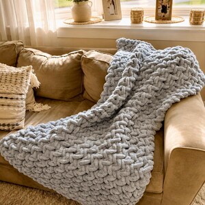 Beginner-friendly chunky hand knit blanket video tutorial by Wistfully Woven featuring the Rustic Barn Weave stitch pattern in a soft sky blue color. Digital PDF download includes a 15+ minute step-by-step YouTube tutorial teaching how to make a cozy chunky knit blanket from cast on to cast off.