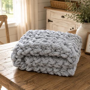 Beginner-friendly chunky hand knit blanket video tutorial by Wistfully Woven featuring the Rustic Barn Weave stitch pattern in a soft sky blue color. Digital PDF download includes a 15+ minute step-by-step YouTube tutorial teaching how to make a cozy chunky knit blanket from cast on to cast off.