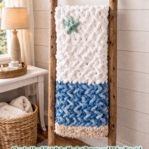 May include: A chunky hand-knit baby blanket in white and blue, draped on a wooden ladder. The blanket features a starfish accent and the text "Beach Bummin' Baby". The blanket is approximately 40 inches wide and 60 inches long.