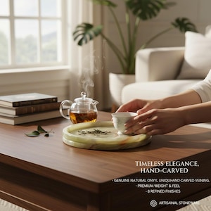 May include: A round, light green, hand-carved natural onyx tray with visible veining. The tray holds loose tea leaves and sits on a wooden surface next to a clear glass teapot with steaming tea and a small white ceramic teacup with floral details.
