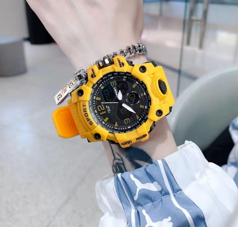 Puede incluir: Un reloj deportivo amarillo y negro con pantalla digital y agujas anal&oacute;gicas. El reloj tiene una correa amarilla y una esfera negra con n&uacute;meros blancos. La palabra "SPORT" est&aacute; impresa en la correa.
