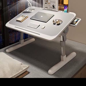 May include: An adjustable laptop desk in white and grey, featuring a built-in lamp, laptop, and keyboard. The desk includes a drawer and is designed for work or study. The desk is supported by a white frame.