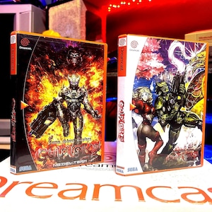 May include: Two Dreamcast video game cases. The case on the left is orange and black with a fiery background and a robot holding a gun. The text on the case reads "Gunlord:  Jump Shoot Exploder, NG.DEV.TEAM". The case on the right is orange and white with a colorful background and a female character in red and black armor. The text on the case reads "Gunlord".