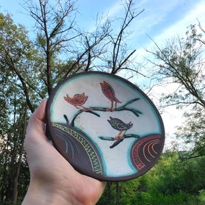 ceramic bird plate held against sky outdoor natural light