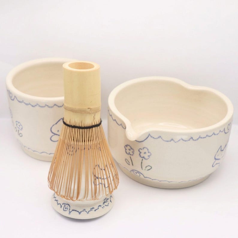 Puede incluir: Un juego de t&eacute; matcha con un batidor de bamb&uacute;, un cuenco peque&ntilde;o y un cuenco m&aacute;s grande con boquilla. Las piezas de cer&aacute;mica son de color blanco roto con dise&ntilde;os azules de olas y flores. El batidor es de bamb&uacute; claro.