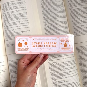 May include: A pink and orange ticket for the Stars Hollow Autumn Festival. The ticket has a pumpkin patch design and the text "It's just my favorite time of the year" and "Stars Hollow Autumn Festival".