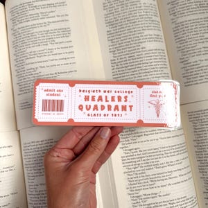 May include: A pink and white bookmark with the text "Basgiath War College* Healers Quadrant* Class of 1013" and a barcode that says "admit one student".