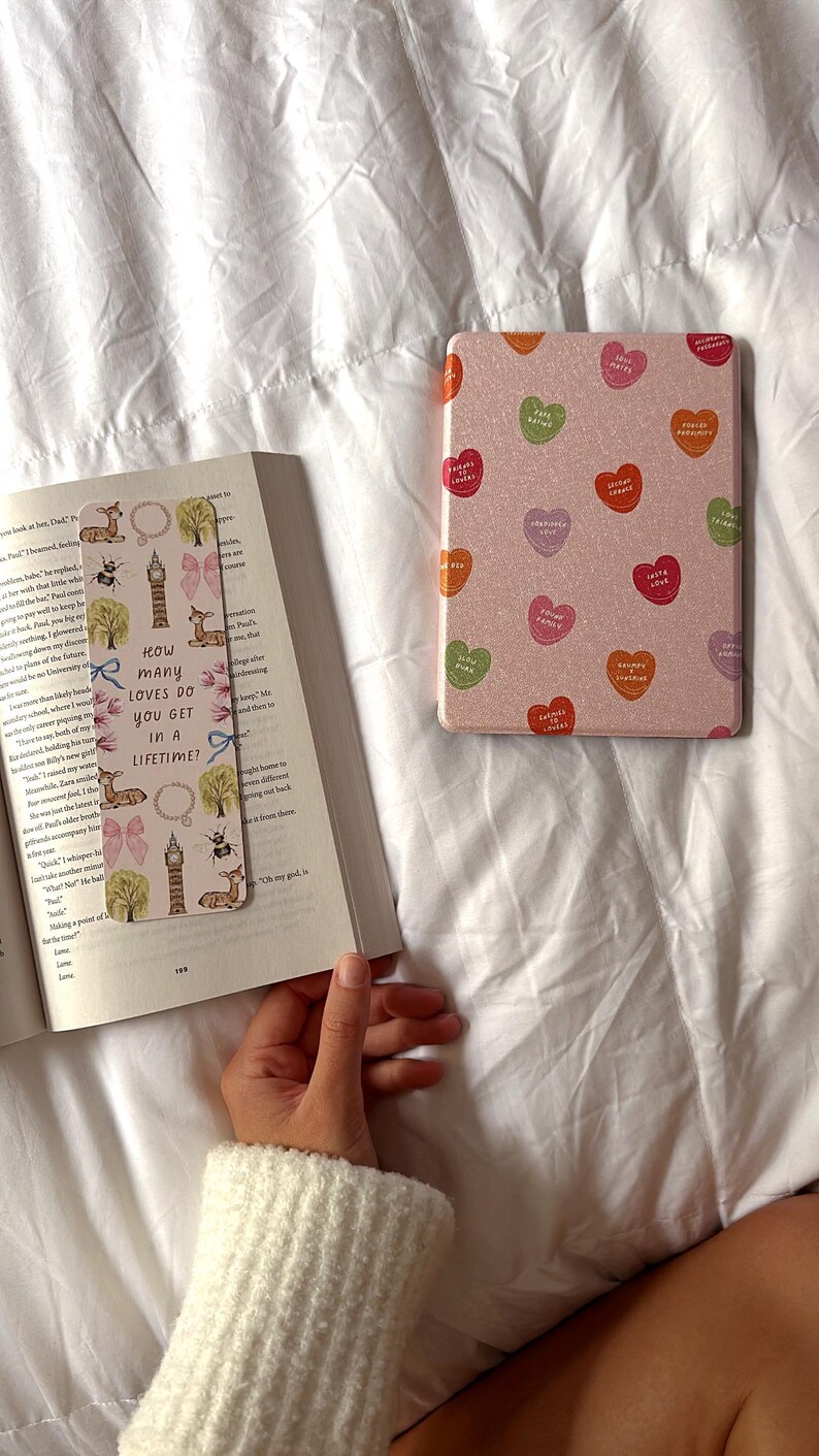 Puede incluir: Un marcap&aacute;ginas rosa con fondo blanco e ilustraciones coloridas de un ciervo, una abeja, una torre del reloj y un &aacute;rbol. El marcap&aacute;ginas tiene el texto "&iquest;Cu&aacute;ntos amores se consiguen en una vida?" impreso en &eacute;l.