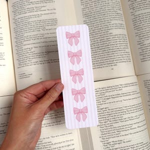 May include: Pink and white bookmark with five pink bows on a white background with pink stripes.