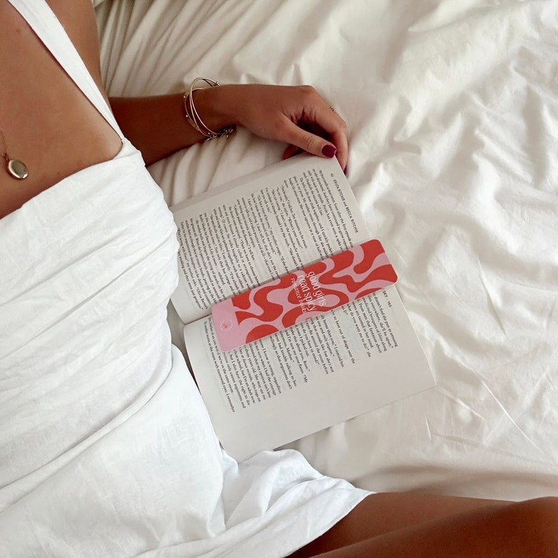 May include: A pink and red bookmark with the text "Sound Girls Read Space" and a wavy abstract design. The bookmark is placed in a book.