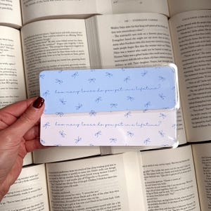 May include: A set of two blue and pink bookmarks with a white background. The bookmarks have a repeating pattern of blue bows and the text "How many loves do you get in a lifetime?" printed in blue.