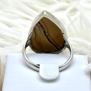 May include: A silver ring with a large, teardrop-shaped stone displaying a brown and black pattern. The ring has a polished silver band and a simple design, suitable for everyday wear.