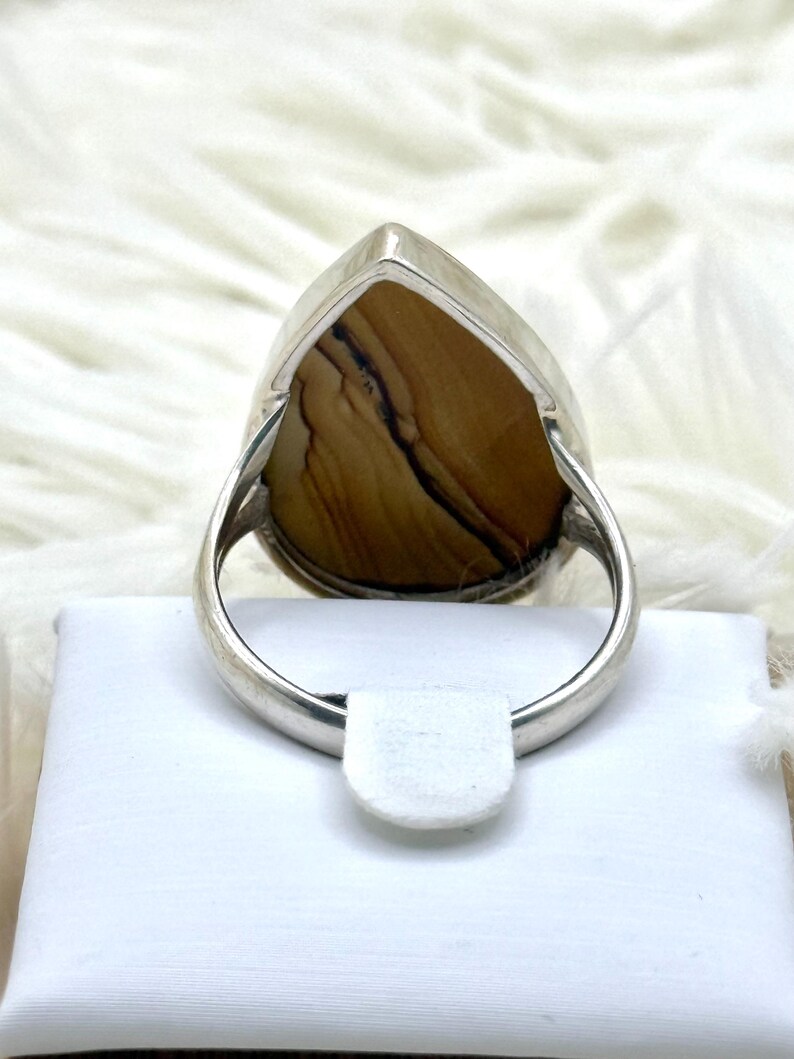 May include: A silver ring with a large, teardrop-shaped stone displaying a brown and black pattern. The ring has a polished silver band and a simple design, suitable for everyday wear.