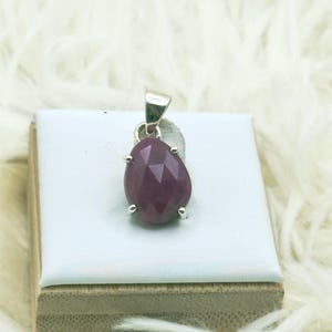 May include: A teardrop-shaped, faceted dark pink gemstone pendant set in a silver-toned metal prong setting. The pendant features a polished silver bail at the top, designed for attachment to a necklace chain, showcasing a deep, saturated color.