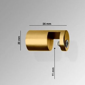 May include: A gold-colored, cylindrical metal object with a curved cutout and a screw. The object is 26 mm long, 20 mm high, and the cutout is 11 mm deep. The object is likely a furniture or cabinet hardware component.