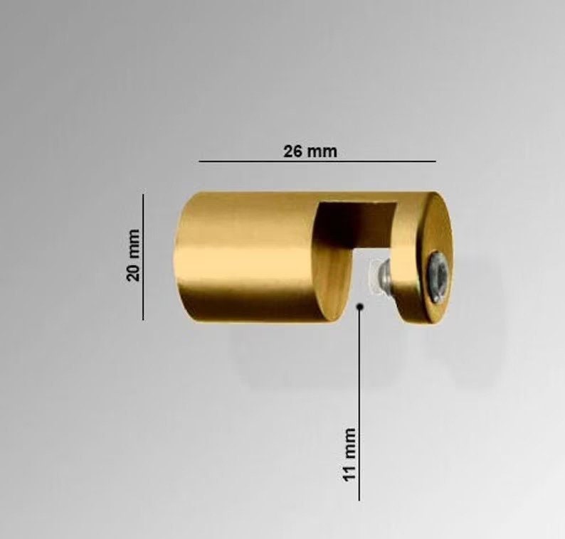 May include: A gold-colored, cylindrical metal object with a curved cutout and a screw. The object is 26 mm long, 20 mm high, and the cutout is 11 mm deep. The object is likely a furniture or cabinet hardware component.