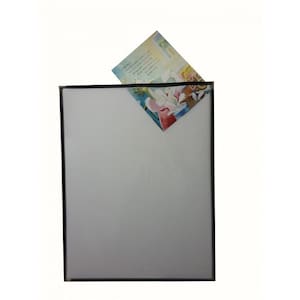 Op de afbeelding: Een witte, vierkante fotolijst met een zwarte rand. Een kleurrijke illustratie is gedeeltelijk zichtbaar, ingevoegd in de hoek van de lijst. De illustratie toont een persoon in een rode en witte outfit.
