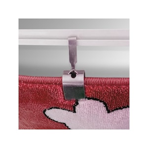 May include: A silver metal hook clip for hanging a rug or tapestry on a rod. The hook is attached to a white rod and is holding a red and pink rug with a white design.
