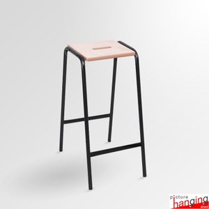 May include: A black metal stool with a light pink wooden seat. The seat has a small cutout in the center.