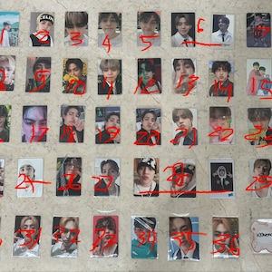 May include: A collection of 36 small, rectangular trading cards, each featuring a different person. The cards are in clear plastic sleeves and numbered with red marker. The background is a light beige surface.