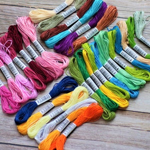 Puede incluir: Una colección de hilos de bordar coloridos en varios tonos, incluyendo rosas, azules, verdes y amarillos. Los carretes están cuidadosamente dispuestos sobre una superficie de madera, mostrando los vibrantes hilos. Ideal para bordado y otros proyectos de manualidades.