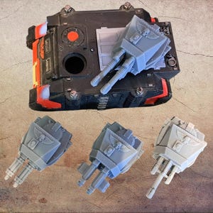 May include: A black and red miniature tank model with a circular hatch and a grey turret attachment. Below the tank are three additional grey turret components, each featuring a winged skull emblem and dual barrel weapon configurations.