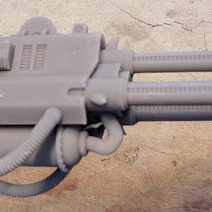 May include: A gray, unpainted resin miniature weapon component featuring a mechanical design with dual barrels, a central housing with ribbed detailing, external tubing, and a claw-like attachment at the front end of the assembly.