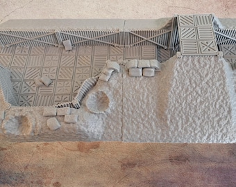 May include: A detailed, light gray miniature diorama of a fortress or building section. The model features textured walls, patterned flooring, and architectural details like a ramp and support beams. The overall design suggests a fantasy or historical theme.