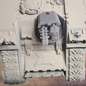 Può includere: Un modello di carro armato in miniatura grigio chiaro con cingoli dettagliati, una torretta e un sistema d'arma. Il modello presenta disegni e trame intricati, che suggeriscono un tema militare o fantascientifico. L'estetica generale è industriale e dettagliata.