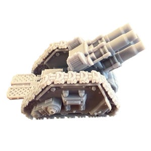 Puede incluir: Un modelo de tanque de plástico gris con un cañón grande de tres cañones montado en la parte superior. El tanque tiene orugas a ambos lados y una pequeña plataforma en la parte delantera.