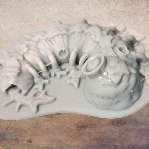 May include: A light grey, unpainted resin miniature of a segmented, worm-like creature with multiple legs and a large, bulbous head section. The figure is sculpted with intricate, organic textures and rests on an integrated, irregular oval base.