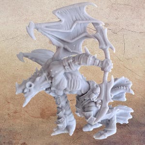 May include: A light grey, 3D-printed miniature of a fantasy creature, possibly a demon or dragon, with large wings, armour, and a sword. The figure is in a dynamic pose, suggesting movement, against a neutral background.
