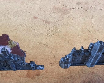 May include: Two miniature, weathered, gray and black castle ruins with red and white accents and patches of green moss. The pieces are set against a textured, tan background.