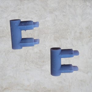 May include: Two blue plastic plumbing connectors with two openings on each side. The connectors are shaped like the letter 'E'.