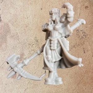 May include: A grey miniature figurine of a female warrior, holding a scythe-like weapon. The figure is detailed with armour, a flowing cape, and a determined expression, ideal for tabletop gaming or collecting.