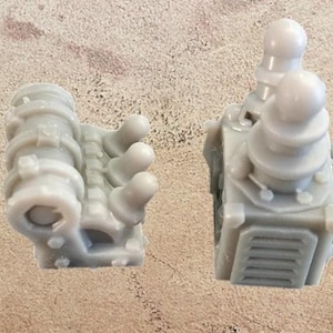 May include: Two light grey miniature model components. One is a cylindrical shape with a series of rings and a hand-like structure with three rounded protrusions. The other is a boxy structure with a series of rounded protrusions.