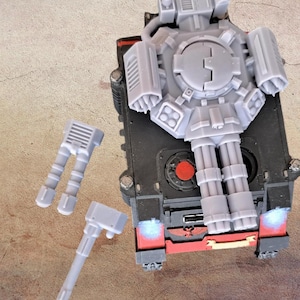 Può includere: Un modello di carro armato nero e rosso con componenti grigi, tra cui una grande struttura centrale e due pezzi di cannone separati. Il carro armato ha accenti rossi e un design dettagliato, che suggerisce un veicolo da guerra in miniatura.